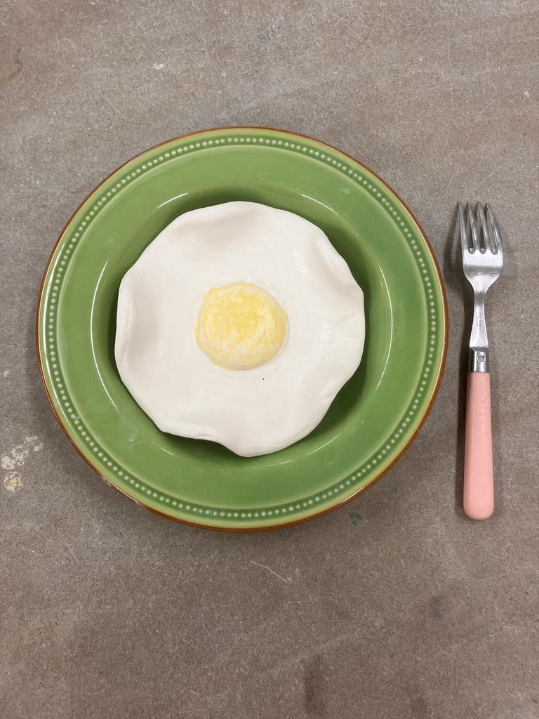 Un oeuf dans une assiette le tout réalisé en poterie